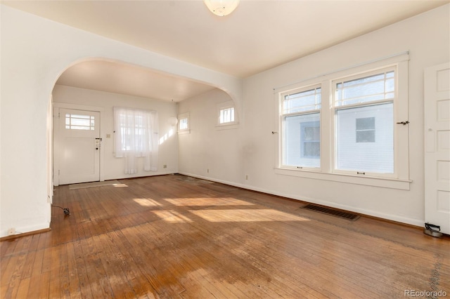 interior space with arched walkways, hardwood / wood-style floors, visible vents, and baseboards