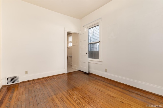 unfurnished room with visible vents, baseboards, and hardwood / wood-style floors