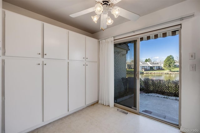 unfurnished bedroom with a water view, access to exterior, a ceiling fan, and visible vents