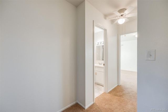 hall with light carpet, a sink, and baseboards