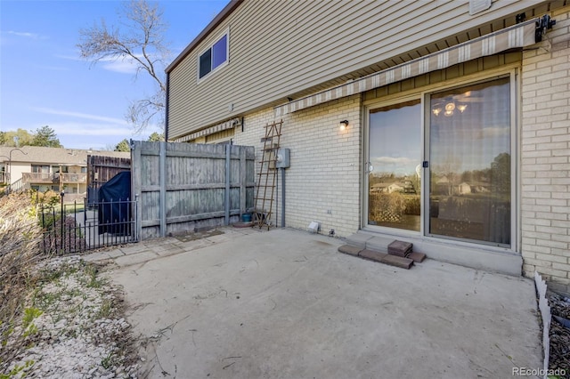 view of side of home with brick siding, a patio, and fence