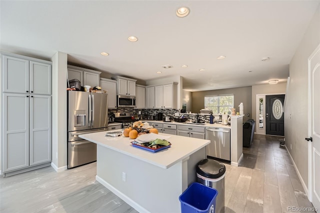 kitchen with a kitchen island, decorative backsplash, a kitchen breakfast bar, stainless steel appliances, and light hardwood / wood-style floors