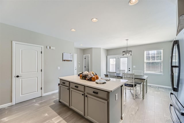 kitchen featuring stainless steel fridge, a kitchen island, pendant lighting, gray cabinetry, and light hardwood / wood-style floors