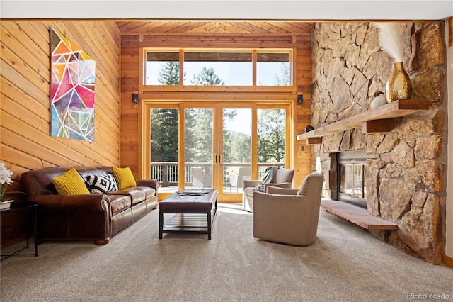 carpeted living room with a stone fireplace and wooden walls