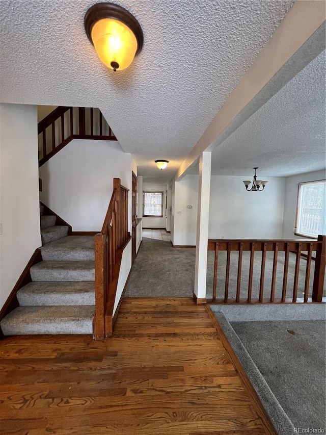 stairway with wood-type flooring, a textured ceiling, and an inviting chandelier