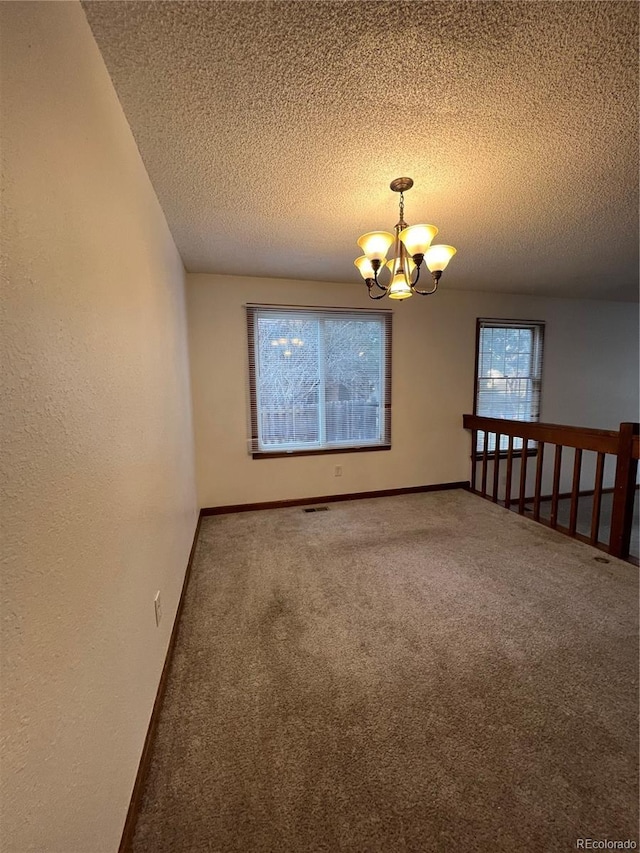 spare room featuring carpet floors, a textured ceiling, and a notable chandelier