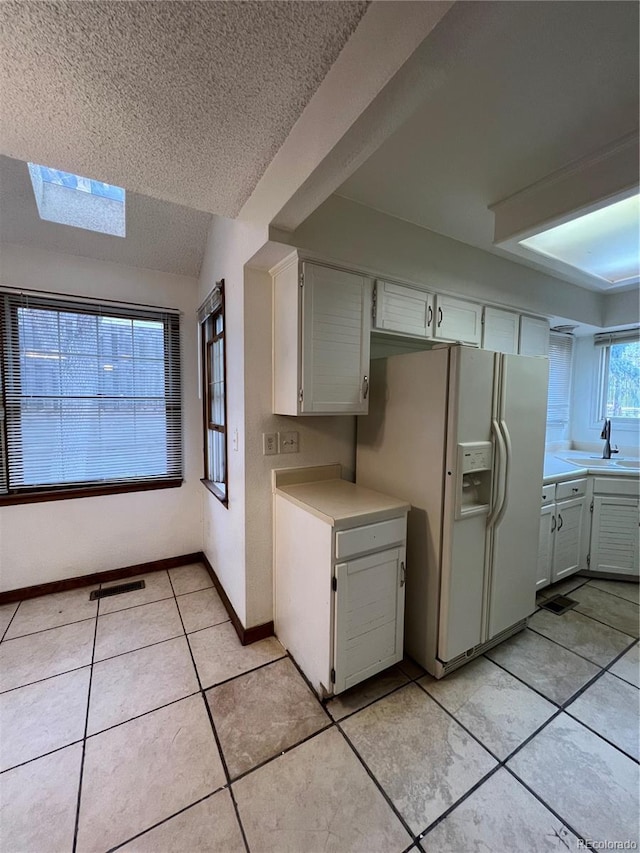 kitchen with sink, white cabinets, white refrigerator with ice dispenser, lofted ceiling with skylight, and light tile patterned floors