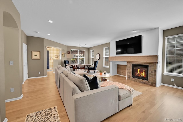 7064 E 2nd Ave, Denver, CO 80220 - living room with arched walkways, light wood finished floors, baseboards, a chandelier, and a tile fireplace