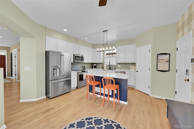 7064 E 2nd Ave, Denver, CO 80220 - kitchen with appliances with stainless steel finishes, light wood finished floors, white cabinets, a kitchen bar, and recessed lighting