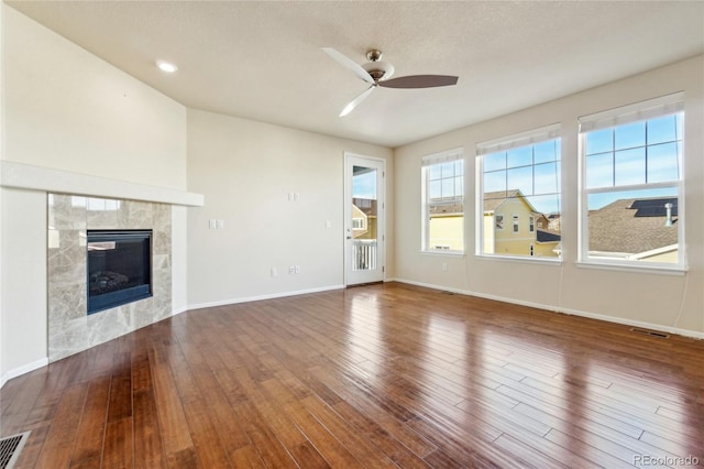 unfurnished living room with visible vents, baseboards, ceiling fan, a tiled fireplace, and wood finished floors