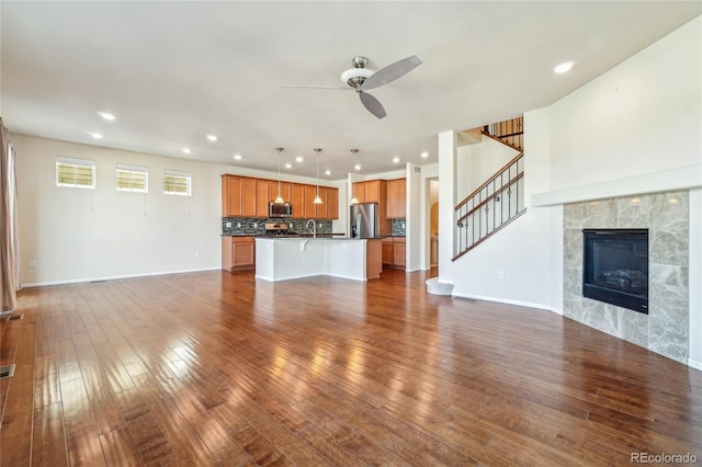 unfurnished living room with dark wood-style floors, baseboards, ceiling fan, and stairway