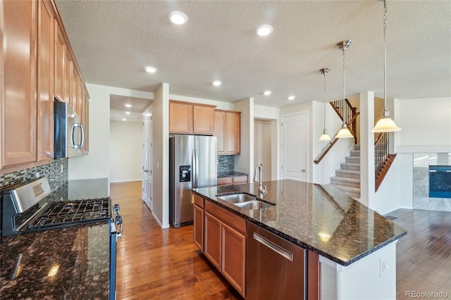 kitchen featuring a sink, a center island with sink, dark stone countertops, stainless steel appliances, and wood-type flooring