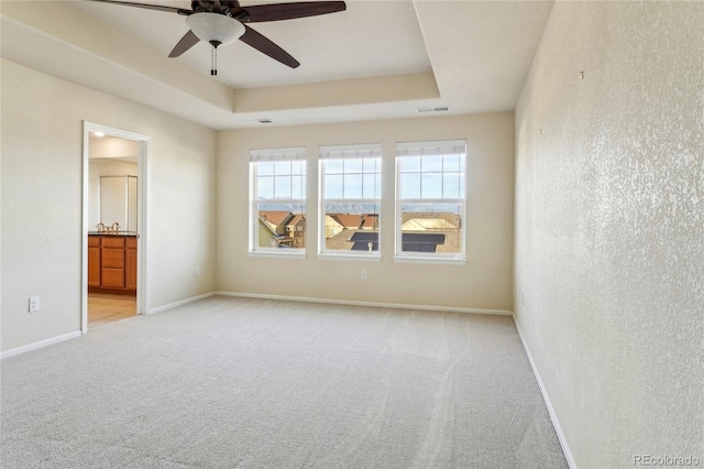 spare room with visible vents, light carpet, a raised ceiling, a ceiling fan, and baseboards