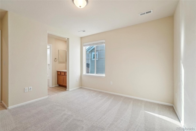 unfurnished bedroom with visible vents, baseboards, light colored carpet, and ensuite bathroom