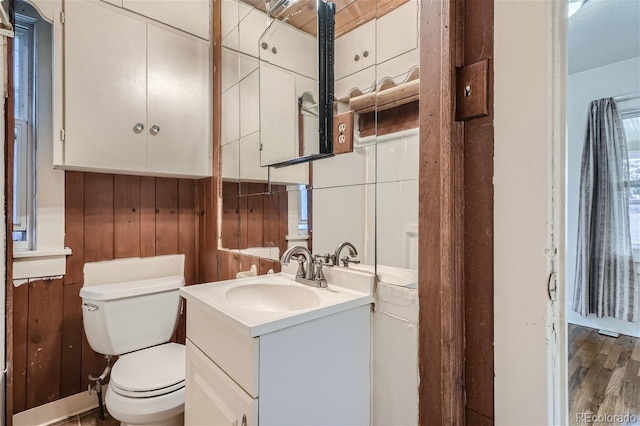 bathroom featuring wood-type flooring, toilet, vanity, and wooden walls