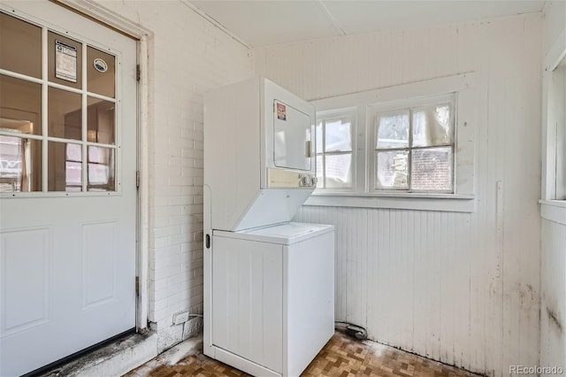 washroom with wooden walls, brick wall, stacked washing maching and dryer, and parquet flooring