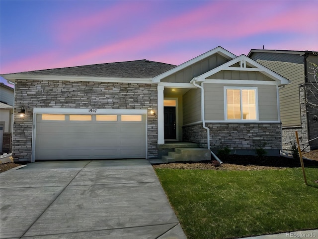 1957 S Coolidge Way, Aurora, CO 80018 - view of front of house with board and batten siding, driveway, an attached garage, stone siding, and a yard