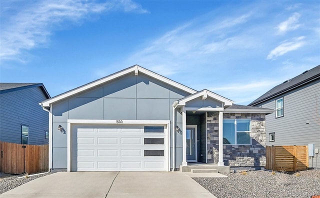 view of front of property with stone siding, a garage, fence, and concrete driveway