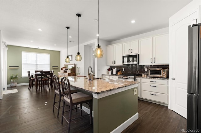 kitchen featuring refrigerator, an island with sink, a breakfast bar area, white cabinets, and light stone counters