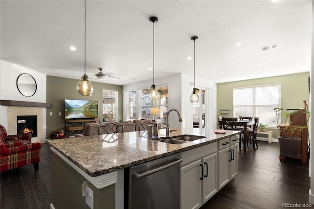 kitchen featuring sink, decorative light fixtures, stainless steel dishwasher, an island with sink, and stone counters