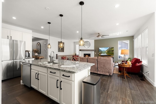 kitchen with sink, appliances with stainless steel finishes, a kitchen island with sink, light stone counters, and white cabinets