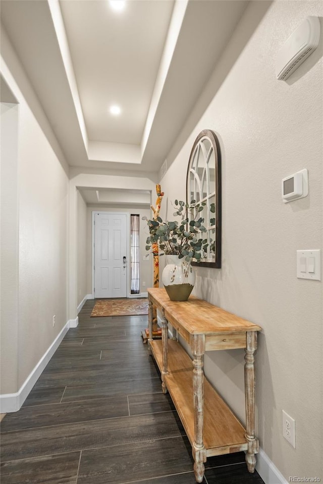 hallway with dark hardwood / wood-style flooring, a raised ceiling, and a wall mounted AC