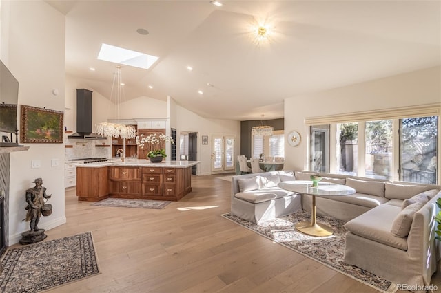 living room with high vaulted ceiling, a skylight, an inviting chandelier, and light wood-style floors