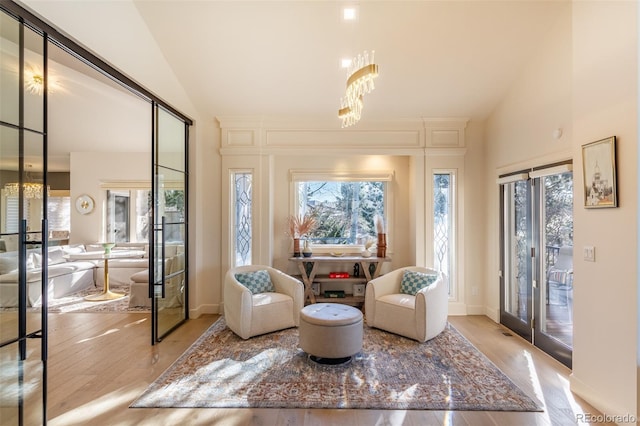 living area with lofted ceiling, light wood finished floors, a chandelier, and a wealth of natural light