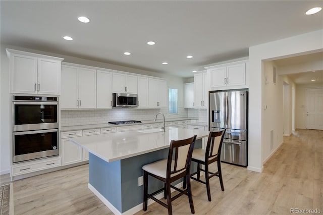 kitchen with stainless steel appliances, a breakfast bar area, decorative backsplash, a center island with sink, and white cabinets