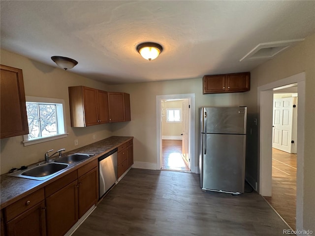 kitchen with a sink, appliances with stainless steel finishes, dark countertops, brown cabinets, and dark wood-type flooring