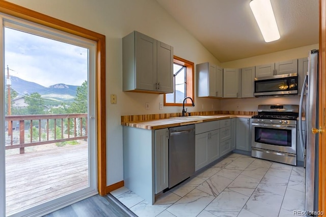 kitchen with lofted ceiling, gray cabinets, a sink, appliances with stainless steel finishes, and marble finish floor