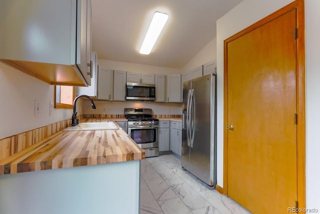 kitchen featuring marble finish floor, gray cabinetry, a sink, wood counters, and stainless steel appliances