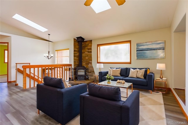 living room featuring ceiling fan with notable chandelier, lofted ceiling with skylight, a wood stove, and wood finished floors