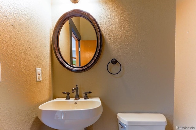 bathroom with toilet, a textured wall, and a sink