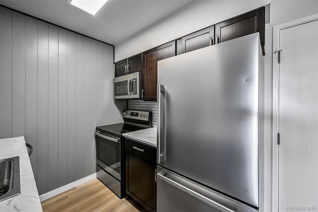 kitchen with stainless steel appliances, light wood-style floors, dark brown cabinets, backsplash, and a sink