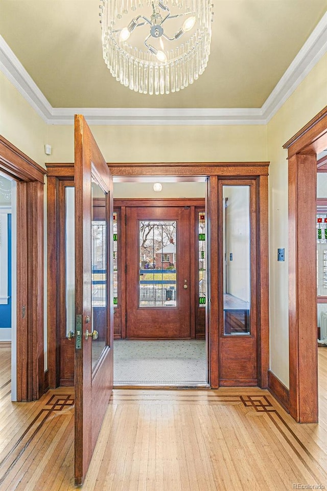 entryway featuring ornamental molding, a notable chandelier, light wood-type flooring, and french doors