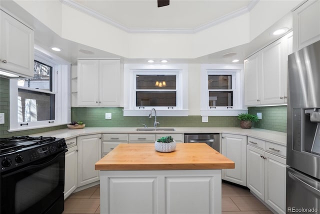 kitchen featuring appliances with stainless steel finishes, butcher block countertops, white cabinetry, sink, and a center island