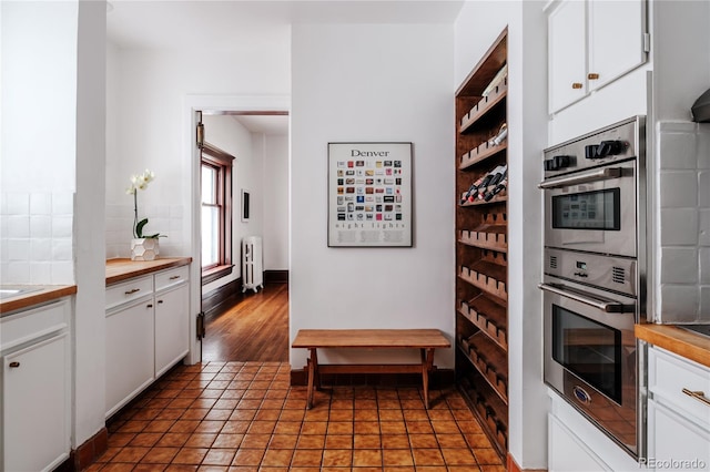 kitchen with white cabinetry, radiator heating unit, stainless steel double oven, dark hardwood / wood-style floors, and butcher block countertops