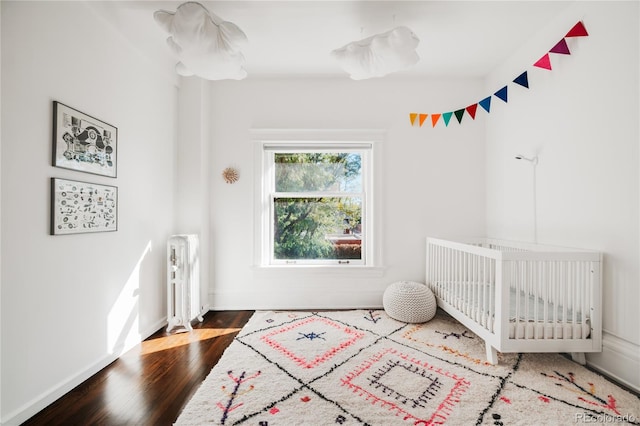 bedroom featuring hardwood / wood-style floors, a crib, and radiator heating unit