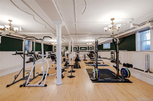 exercise room with radiator heating unit, ornate columns, hardwood / wood-style floors, and a notable chandelier