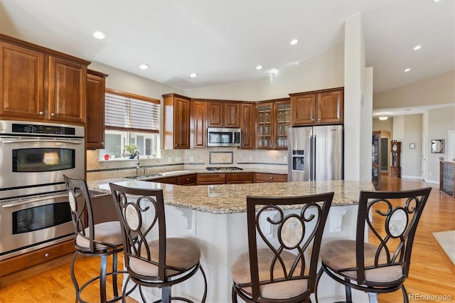 8714 E 148th Cir, Thornton, CO 80602 - kitchen featuring light stone countertops, a kitchen bar, vaulted ceiling, stainless steel appliances, and backsplash