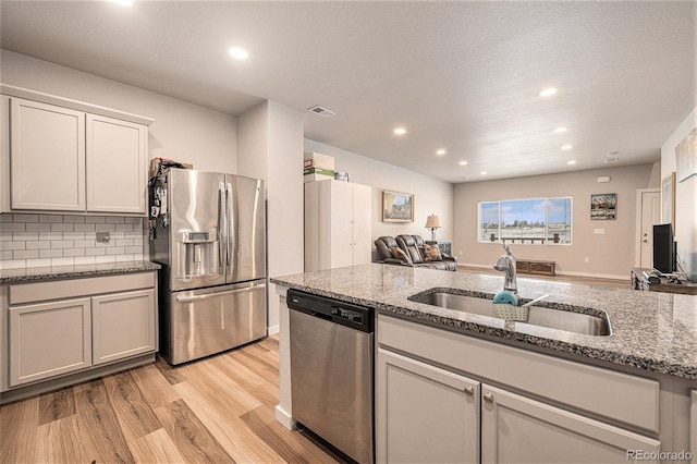 kitchen with stainless steel appliances, sink, light stone counters, and light wood-type flooring