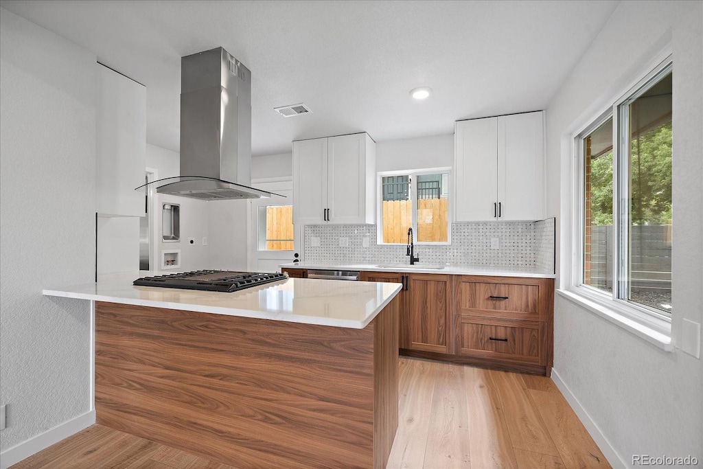 kitchen featuring stainless steel gas stovetop, island exhaust hood, light hardwood / wood-style floors, and white cabinetry