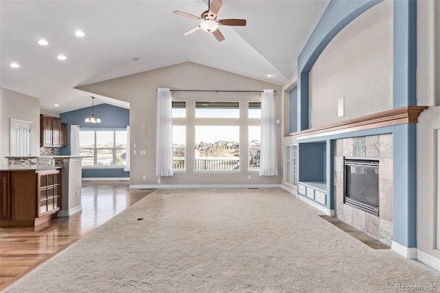 unfurnished living room featuring baseboards, ceiling fan with notable chandelier, vaulted ceiling, and a tile fireplace