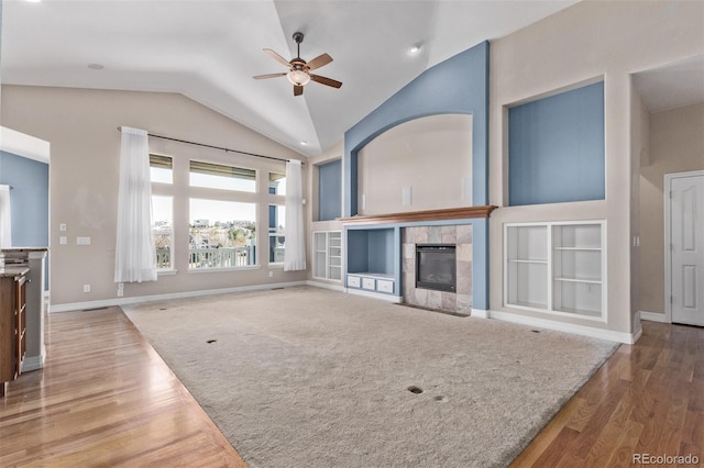 unfurnished living room with lofted ceiling, built in features, wood finished floors, and a tile fireplace