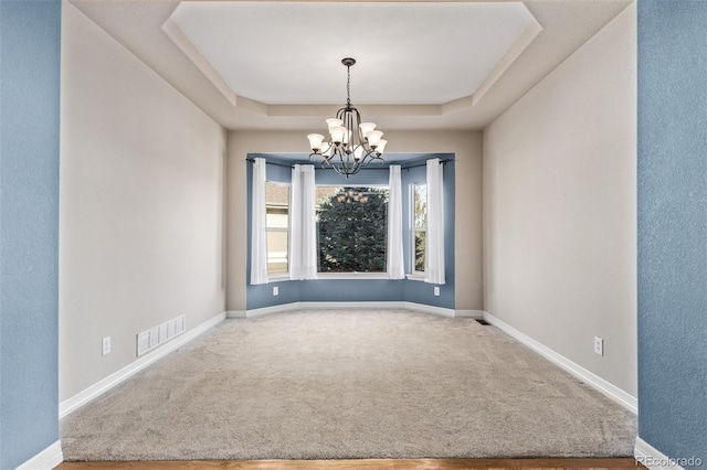 carpeted spare room featuring baseboards, a raised ceiling, visible vents, and an inviting chandelier