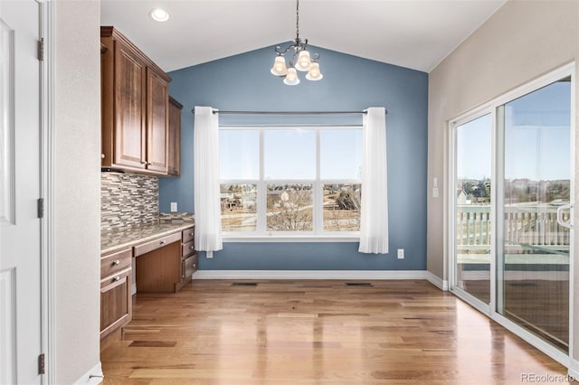 unfurnished dining area featuring light wood finished floors, baseboards, vaulted ceiling, built in desk, and a notable chandelier