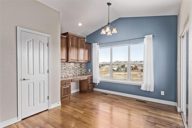 kitchen with pendant lighting, built in desk, light countertops, light wood-style floors, and vaulted ceiling