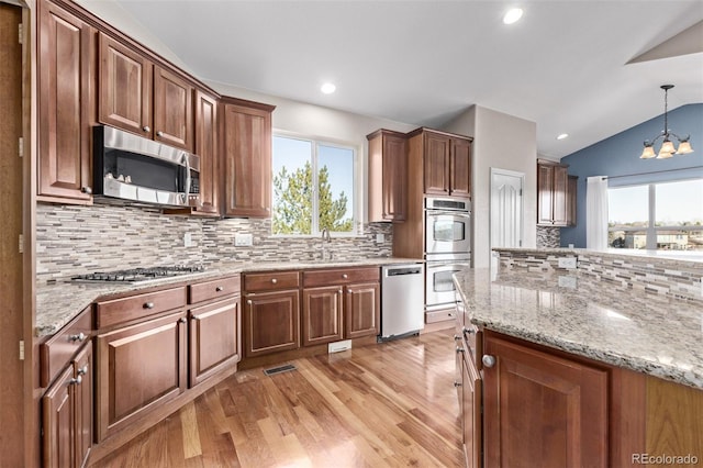 kitchen with pendant lighting, light wood finished floors, an inviting chandelier, appliances with stainless steel finishes, and vaulted ceiling