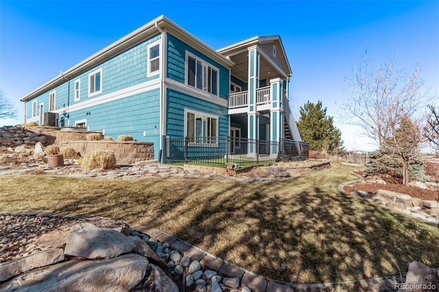 rear view of property featuring a yard, fence, and a balcony